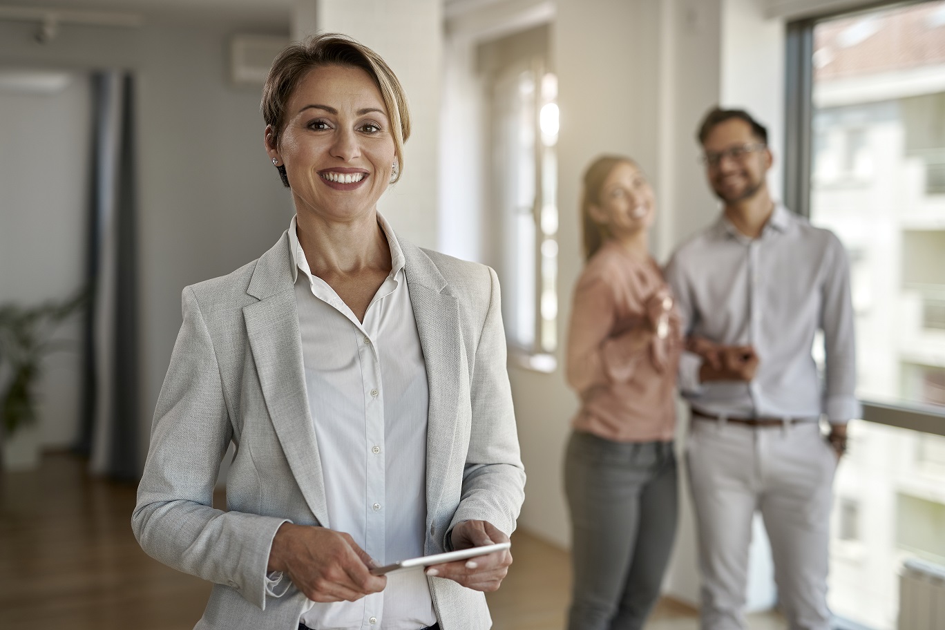 Portrait of happy real estate agent looking at the camera while her clients are standing in the background.